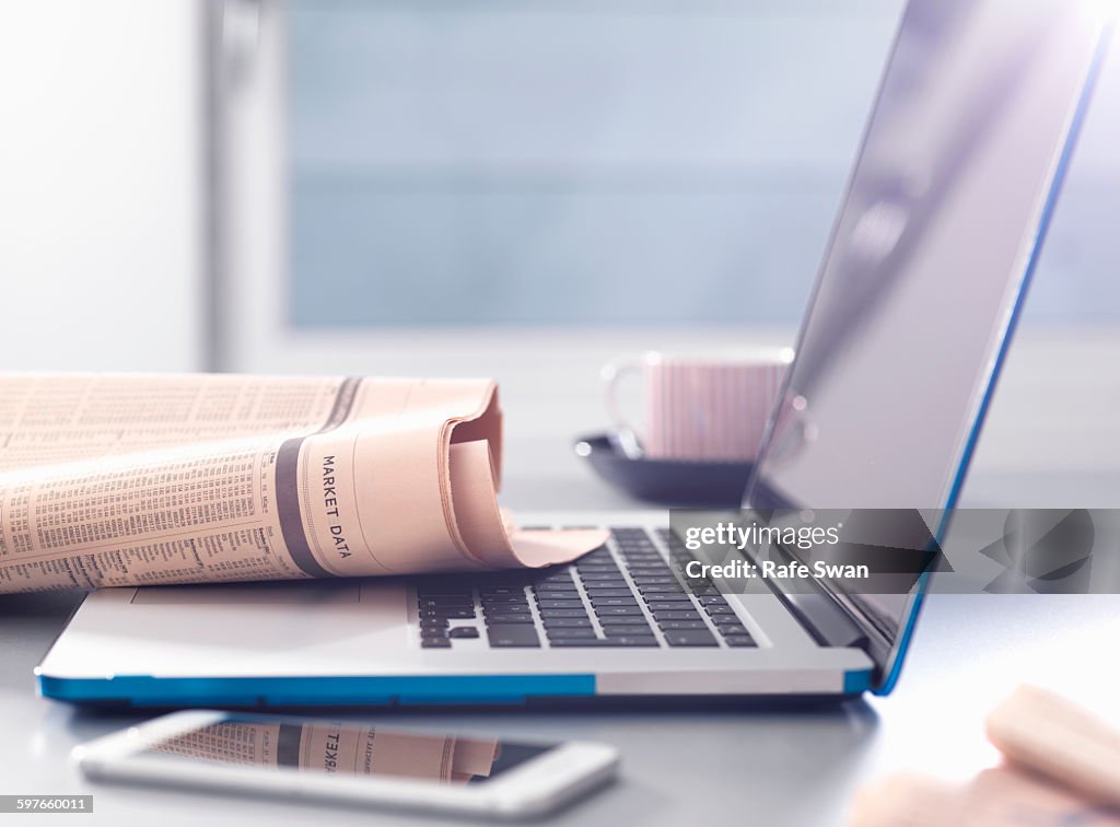 Reviewing financial affairs with newspaper market data page sitting on a laptop computer