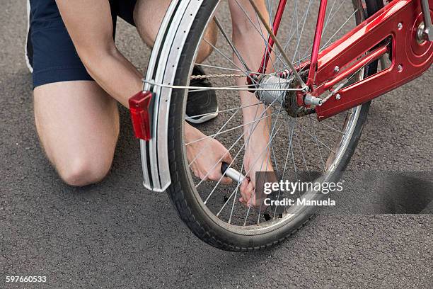 cropped view of young man kneeling inflating bicycle tyre - inflate stock-fotos und bilder