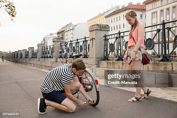 young woman watching young man kneeling inflating bicycle tyre - inflate stock-fotos und bilder