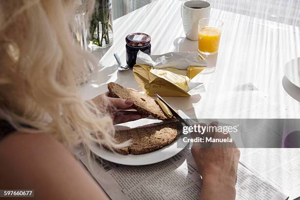 over shoulder view of mature woman spreading butter onto bread - untar de mantequilla fotografías e imágenes de stock