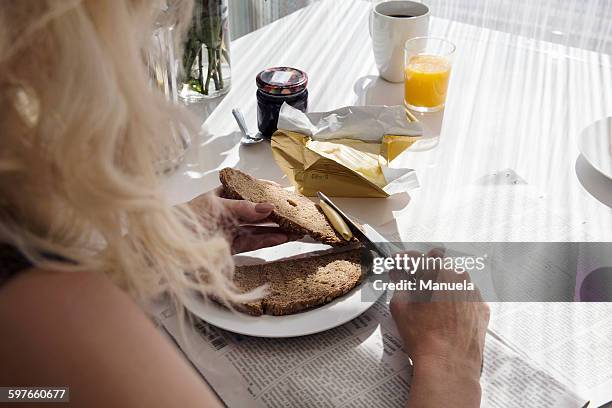 over shoulder view of mature woman spreading butter onto bread - spread over stock pictures, royalty-free photos & images