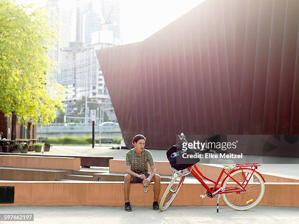 young man taking break beside bicycle, southbank, melbourne, australia - southbank imagens e fotografias de stock