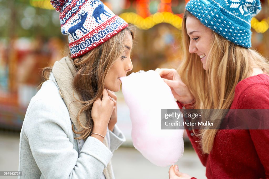 Two young women eating candy floss at funfair, outdoors