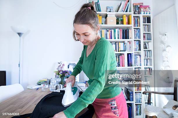 side view of mid adult woman ironing, looking down - trabalho fastidioso - fotografias e filmes do acervo