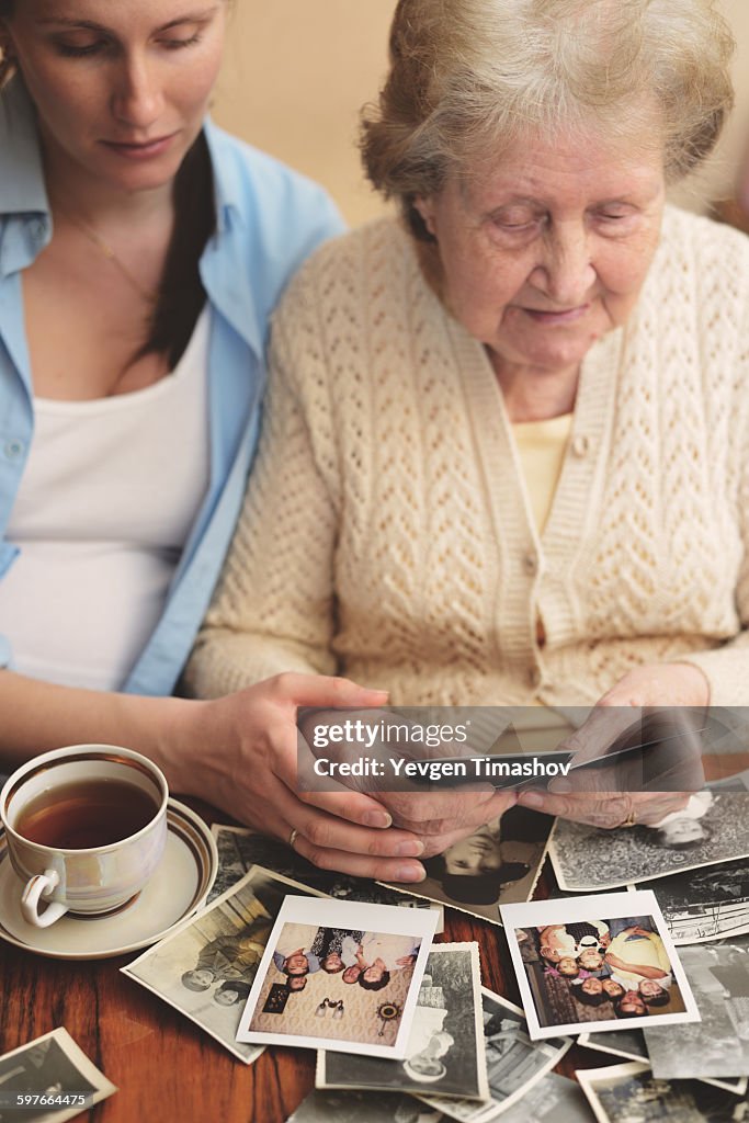 Senior woman and granddaughter sitting at table, looking through old photographs
