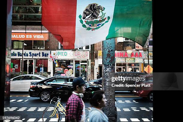 People walk under a Mexican flag in the ethnically diverse neighborhood of Queens on August 29, 2016 in New York City. Queens County is one of the...