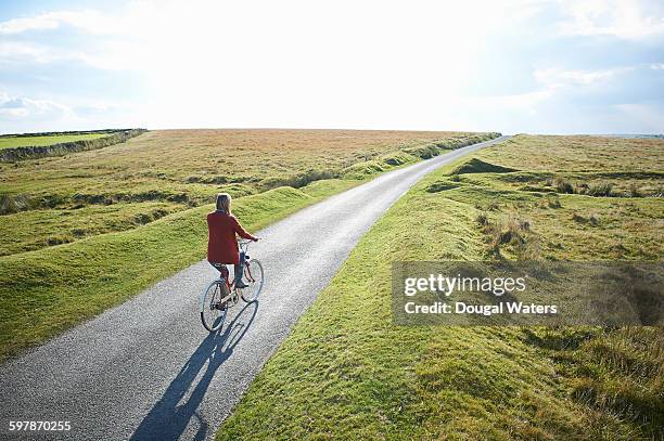 woman riding bike along country lane. - landweg stockfoto's en -beelden