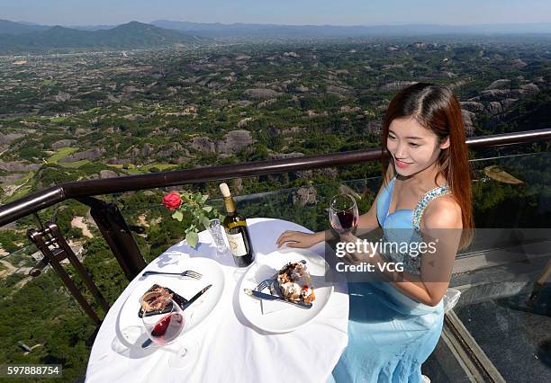 Visitor tastes desserts at an outdoor dining hall on Shiniuzhai's glass-bottomed bridge in Pingshan County on August 29, 2016 in Yueyang, Hunan...