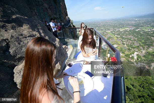 Visitors enjoy desserts at an outdoor dining hall on Shiniuzhai's glass-bottomed bridge in Pingshan County on August 29, 2016 in Yueyang, Hunan...