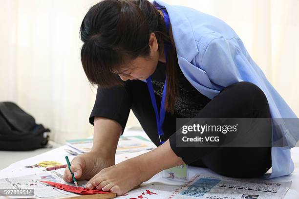 Armless girl Xia Hong traces on red paper with her feet during a handcraft competition on August 29, 2016 in Beijing, China. 232 participants...