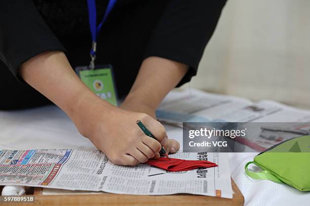 Armless girl Xia Hong traces on red paper with her feet during a handcraft competition on August 29, 2016 in Beijing, China. 232 participants...