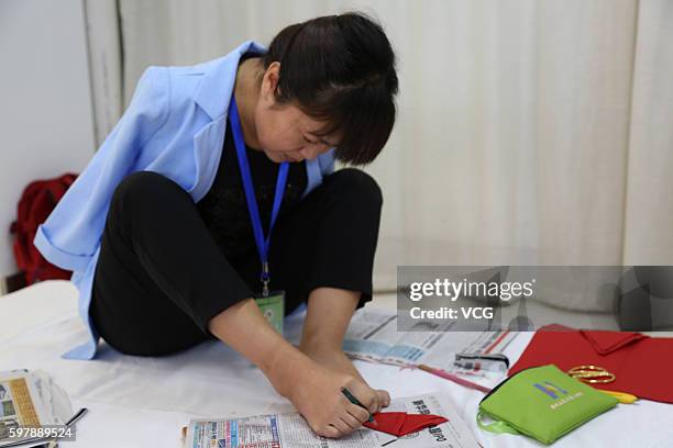 Armless girl Xia Hong traces on red paper with her feet during a handcraft competition on August 29, 2016 in Beijing, China. 232 participants...