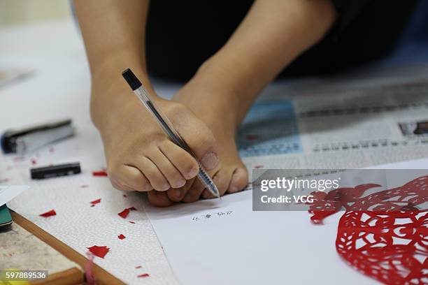 Armless girl Xia Hong writes name of her paper-cutting "Harvest" with her feet during a handcraft competition on August 29, 2016 in Beijing, China....