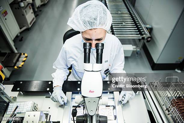 An employee wears protective clothing whilst inspecting a gold wire bonded circuit board using a microscope camera, manufactured by Leica...