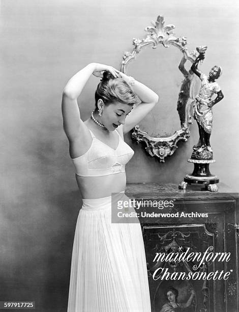 Woman adjusts her hair as she poses in an ad wearing her Maidenform Chansonette bra, 1949.