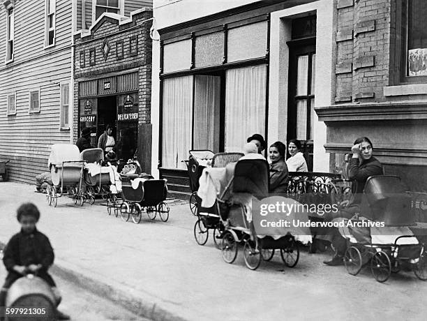 Women and men sitting with baby carriages in front of the Sanger Clinic on Amber Street in Brooklyn, New York, New York, October 1916. It was to...