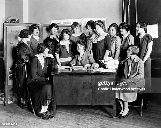 Margaret Sanger seated behind a desk and surrounded by twelve other women, New York, New York, circa 1924.