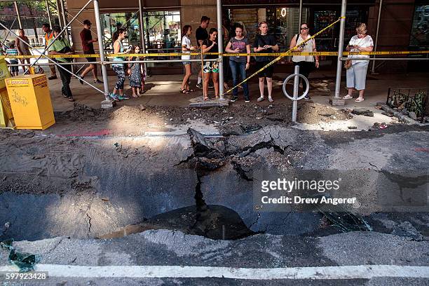 Pedestrians stop and look at a sinkhole caused by a water main break on Amsterdam Avenue, in the Upper West Side section of Manhatten, August 30,...