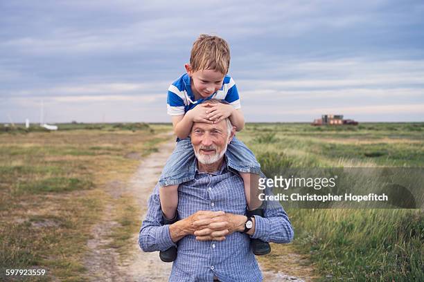 young boy being carried by his grandad - mann mit kind auf den schultern stock-fotos und bilder