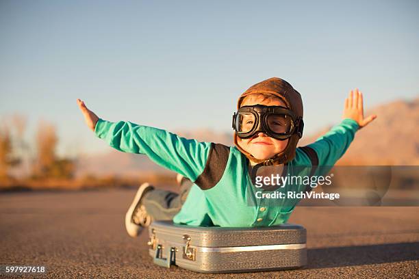 young boy with goggles imagines flying on suitcase - aviation hat 個照片及圖片檔