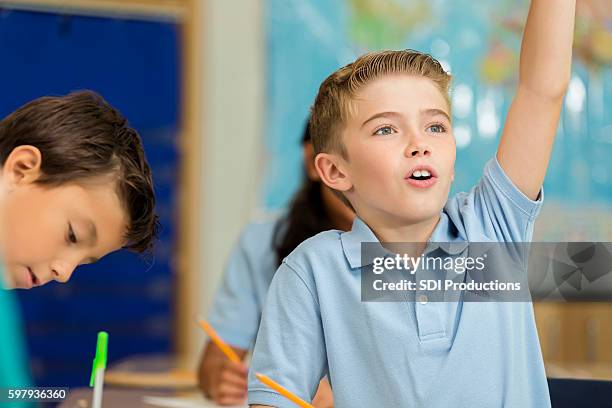 cute caucasian boy raises hand to answer question in class - questions answered stock pictures, royalty-free photos & images