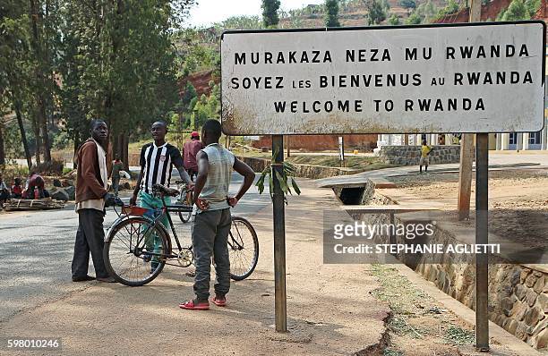 People stand by a placard reading "Welcome to Rwanda" in Akanyaru on the Rwandan side of the street located at the border with Burundi, on August 23,...