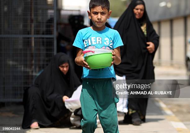 An Iraqi displaced child carries bowls on August 31, 2016 during a food distribution for displaced and impoverished families at the shrine of the...
