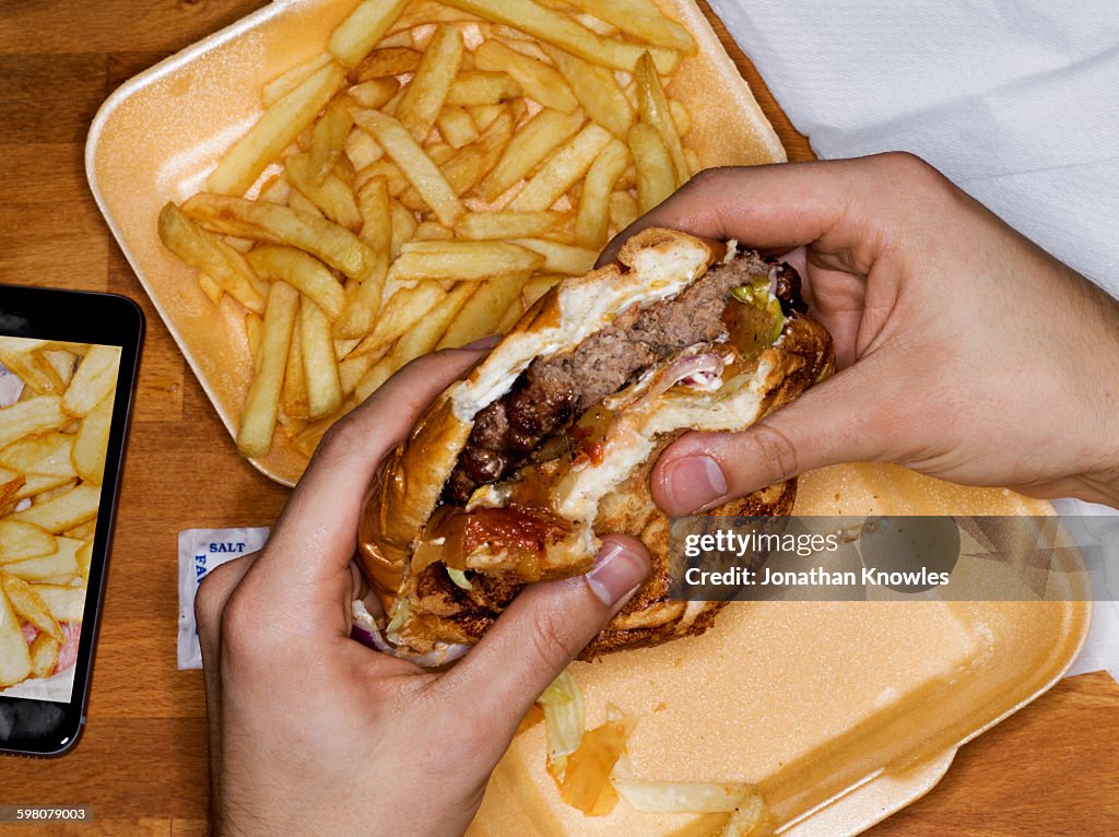 Men eating hamburger and fries, phone with picture