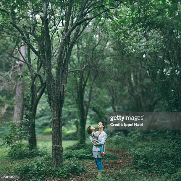 Mother holding her child and looking up at tree canopy