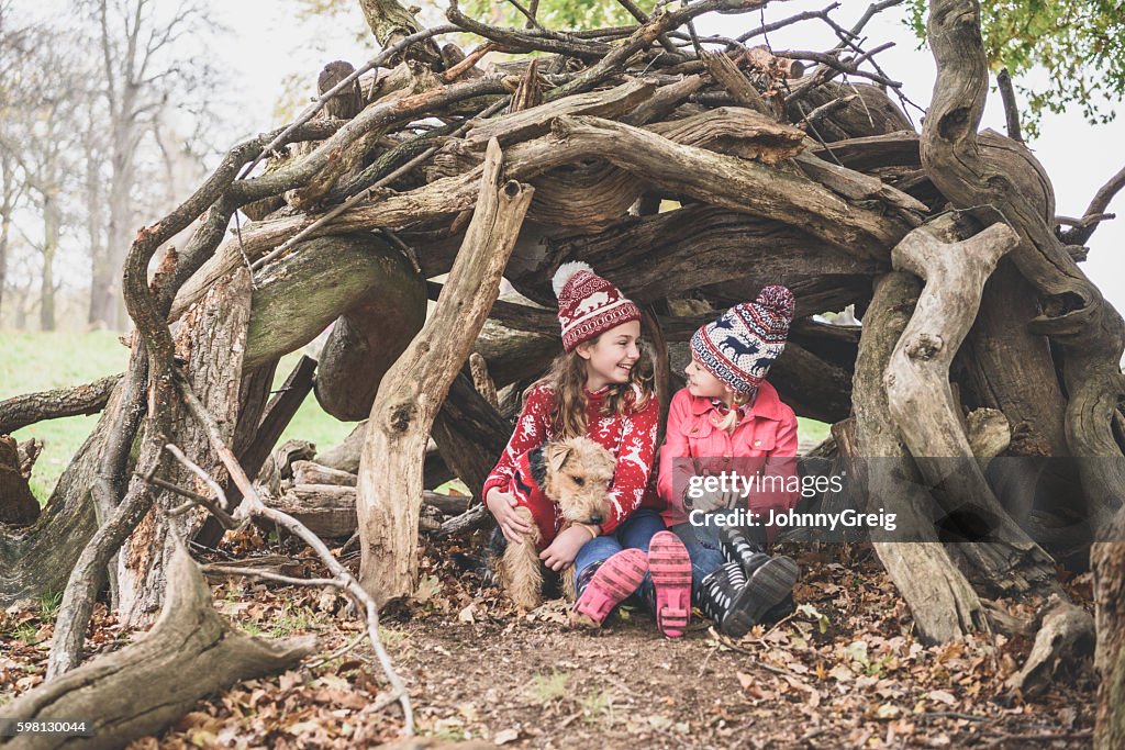 Two sisters in winter clothes in log den with dog