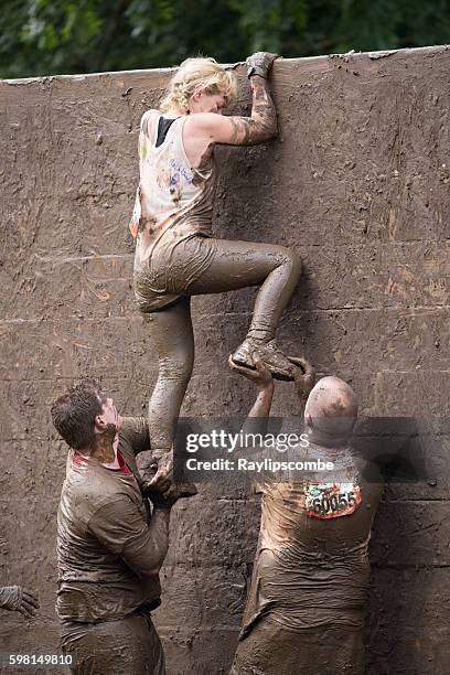 helping hand for a woman climbing a slippery wall - tough mudder imagens e fotografias de stock