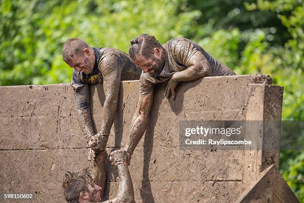 helping hand to climb a slippery wall - toughmudder stock pictures, royalty-free photos & images