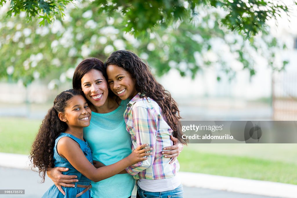 Mother and daughters hugging tightly and smiling at camera