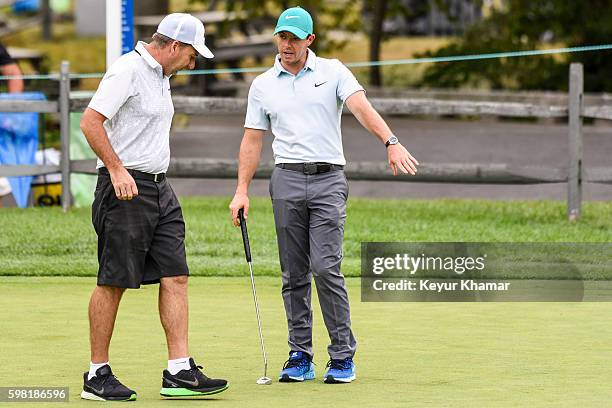 Rory McIlroy of Northern Ireland discusses putting with his caddie J.P. Fitzgerald on the practice green prior to the Deutsche Bank Championship at...