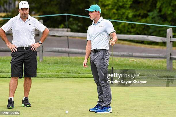 Rory McIlroy of Northern Ireland reacts to his putt on the practice green with his caddie J.P. Fitzgerald prior to the Deutsche Bank Championship at...