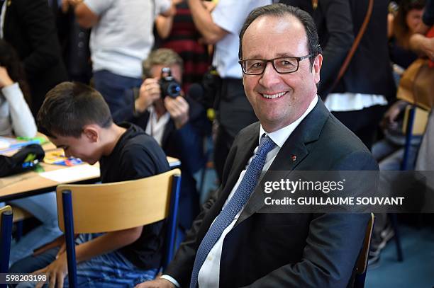 French President Francois Hollande smiles as he sits in a classroom during a visit at the high school Jean Rostand for the first day of the starting...