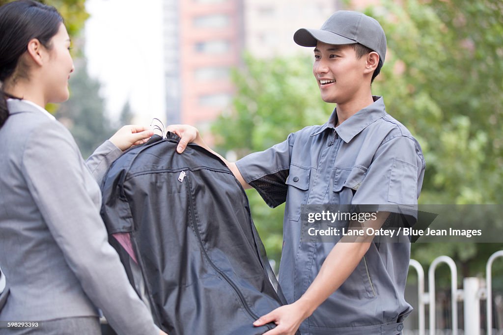Young woman getting dry-cleaned clothes from delivery person