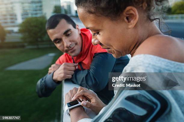 man looking at friend using smart watch while standing by railing at sidewalk - railing stockfoto's en -beelden