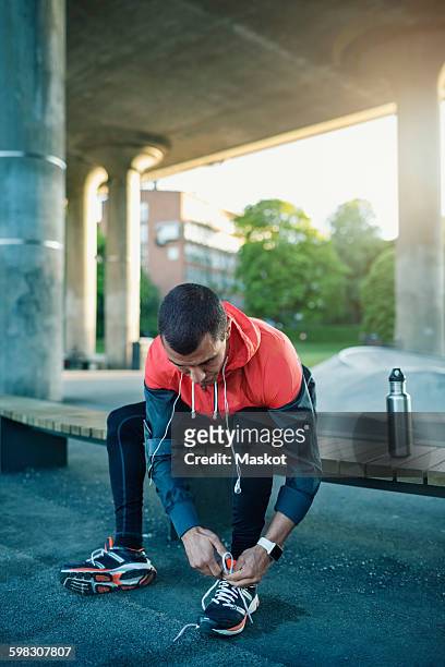man tying shoelace while sitting on bench under bridge - shoelaces ストックフォトと画像