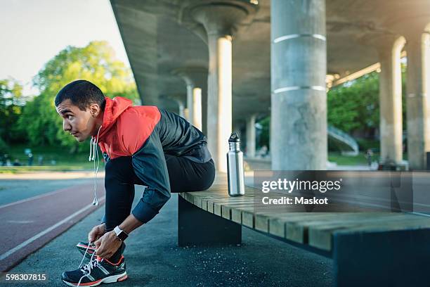 man tying shoelace while sitting on bench - knoten stock-fotos und bilder