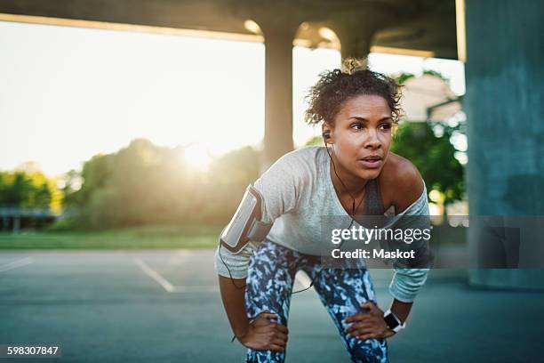 woman listening music bending on street - woman fitness focus stock pictures, royalty-free photos & images