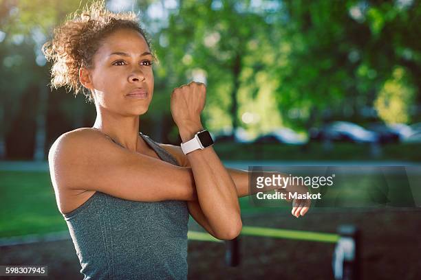 woman wearing smart watch stretching at park - arm span stockfoto's en -beelden