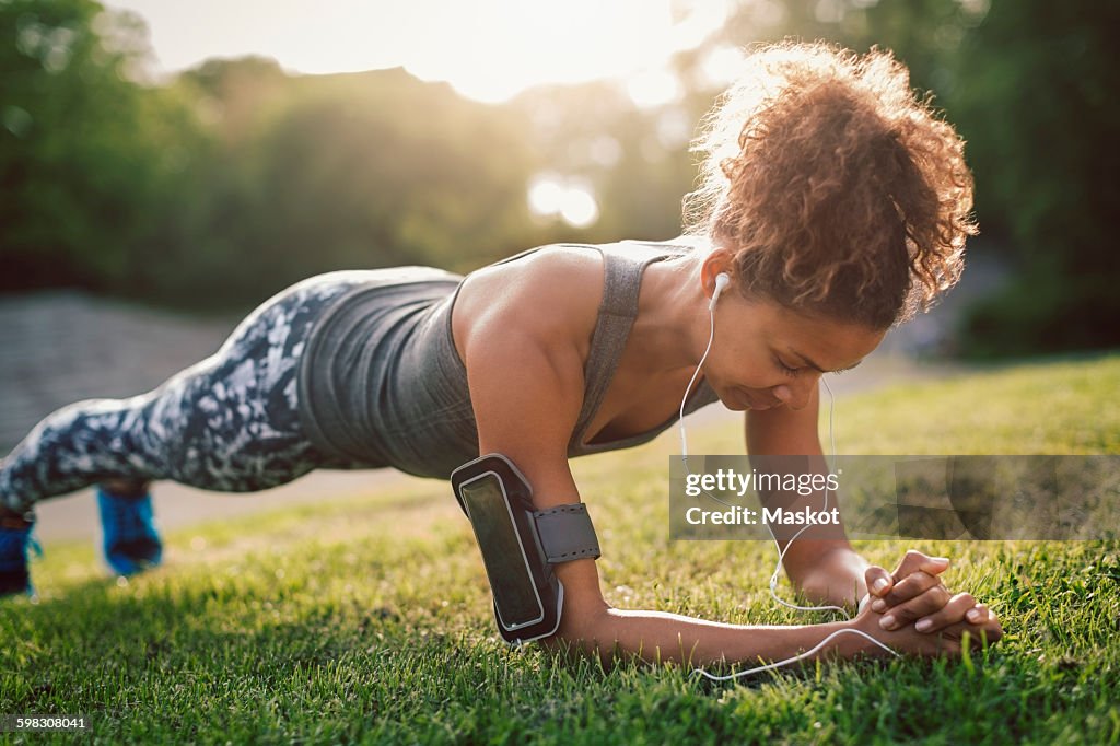 Woman doing plank exercise on grassy field at park