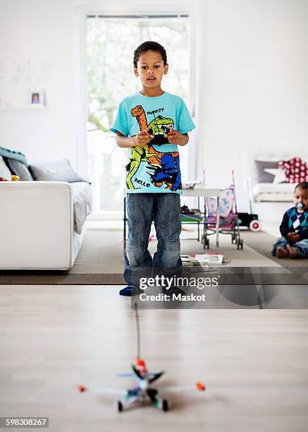 boy playing with remote controlled airplane at home with brother sitting in background - modellflygplan bildbanksfoton och bilder