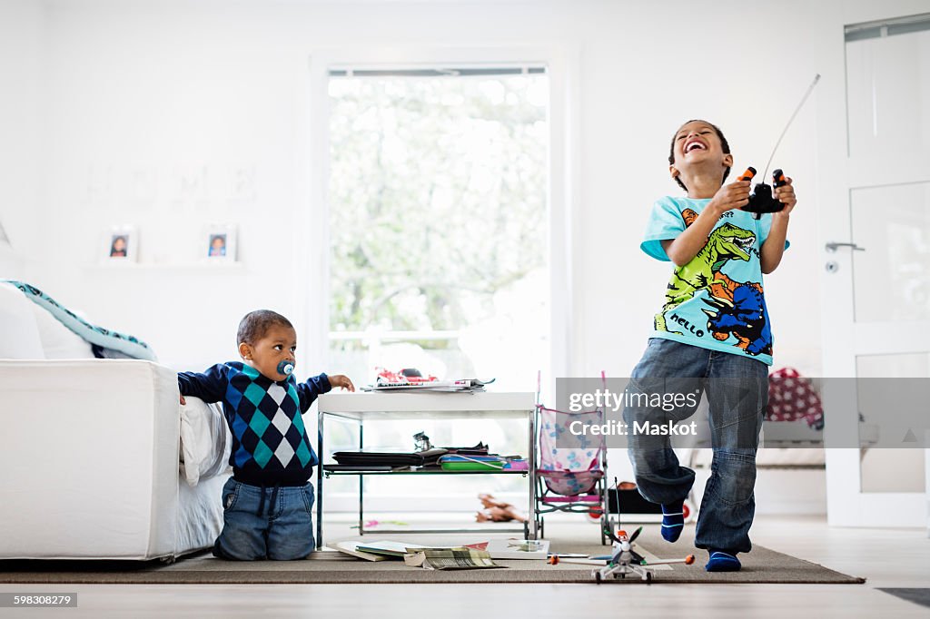 Boy looking at happy brother holding remote of model airplane at home