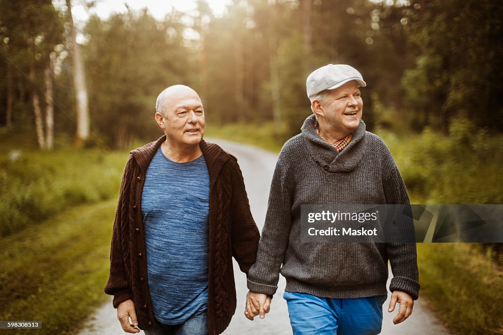 Happy gay couple looking away while walking on road amidst trees
