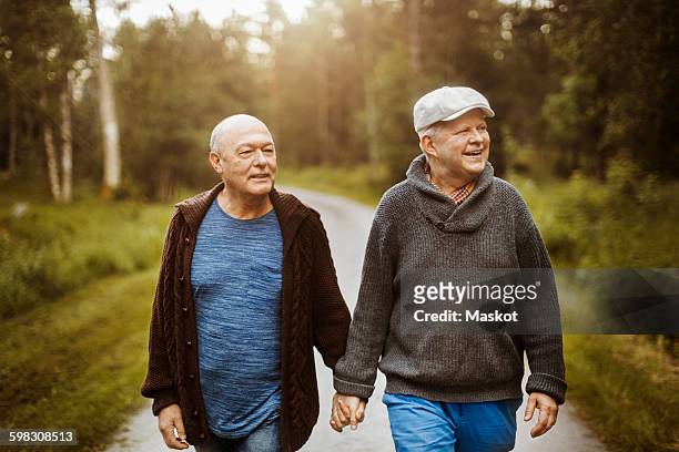 Happy gay couple looking away while walking on road amidst trees