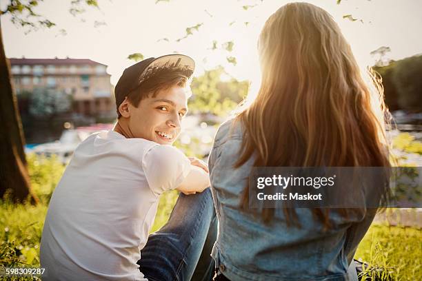 rear view portrait of happy teenager sitting with female friend at lakeshore - junge 13 jahre oberkörper strand stock-fotos und bilder