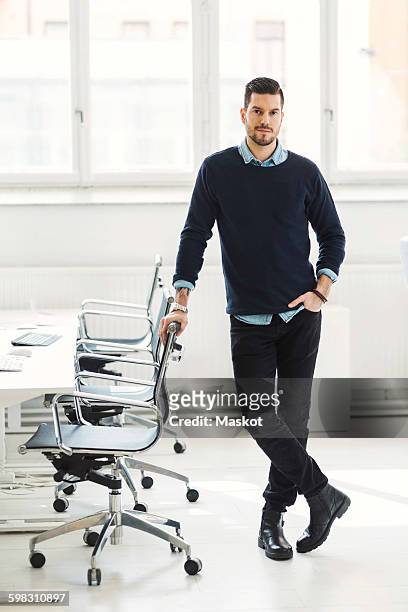 full length portrait of confident businessman leaning on office chair - smart casual stock pictures, royalty-free photos & images