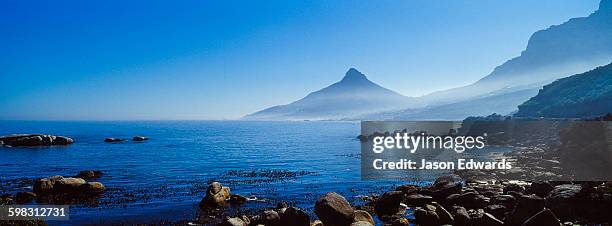 boulders line the shore of table bay looking back on the lions head. - chapmans peak stock pictures, royalty-free photos & images